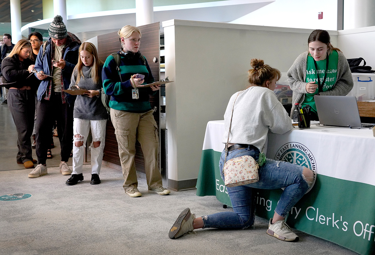 Students kneels at table while registering to vote.